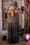 Woman in a long, dark dress standing in a rustic setting with pink lights.