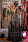Woman in a long, dark dress standing in a room with vintage clothing and props.