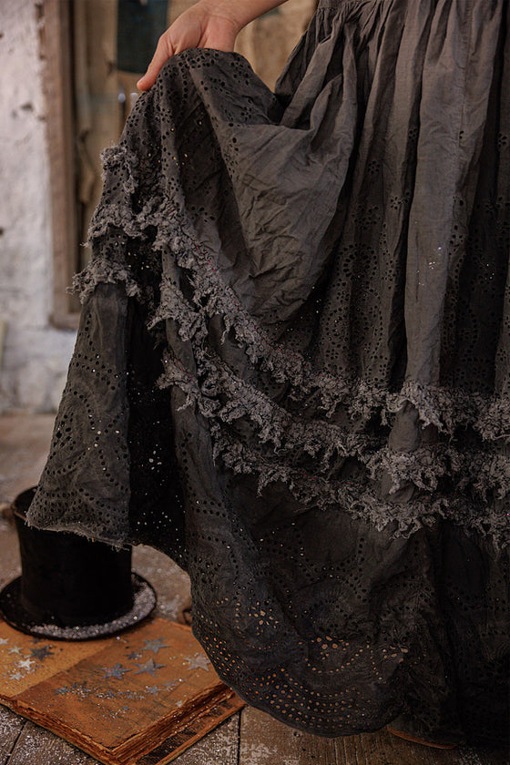 Close-up of a dark, textured fabric with lace details on a rustic wooden floor.