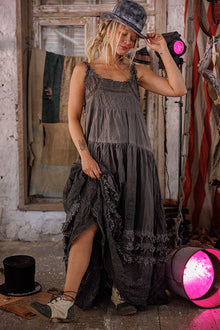  Woman in a long, dark dress standing in a rustic setting with pink lights.