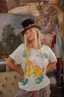  Woman wearing a white t-shirt with a colorful dragon design in a rustic setting.