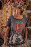 Person wearing a gray t-shirt with a strawberry design and floral headpiece in front of a colorful mural.