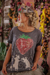 Person wearing a t-shirt with a sequined strawberry design and floral crown in a decorative setting.