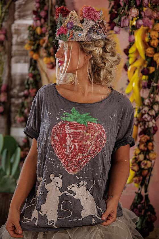 Person wearing a t-shirt with a sequined strawberry design and floral crown in a decorative setting.