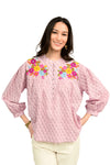 Woman wearing a pink blouse with floral embroidery on a white background