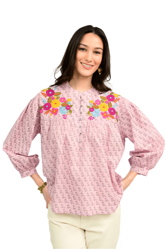 Woman wearing a pink blouse with floral embroidery on a white background