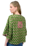 Woman wearing a green patterned top with a pink design on a plain background