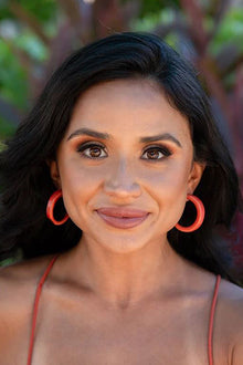 Woman with dark hair and orange hoop earrings against a blurred natural background