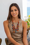 Woman wearing a colorful necklace sitting outdoors with a blurred background