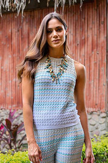  Woman wearing a light blue sleeveless top and patterned pants standing in front of a red wooden wall.