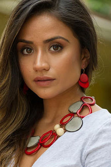  Woman wearing a red and silver necklace with earrings against a blurred background