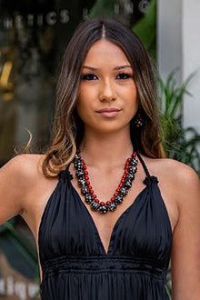  Woman wearing a black dress and red and black beaded necklace in front of a blurred background