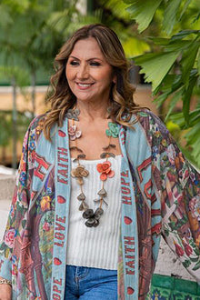  Woman wearing a colorful kimono with text and floral patterns, standing outdoors with greenery.